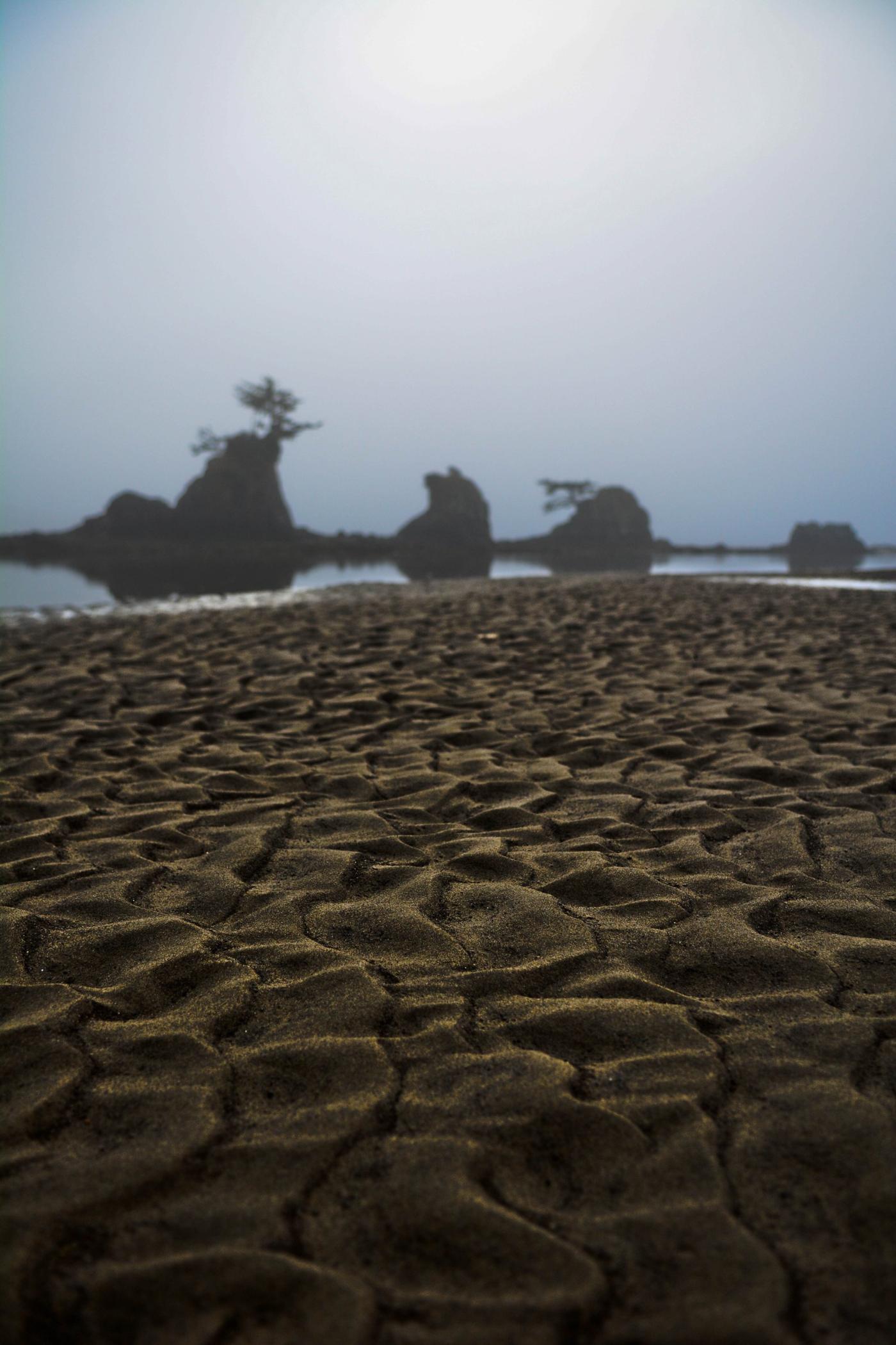 Sea stacks rising from fog above rippled sand at low tide